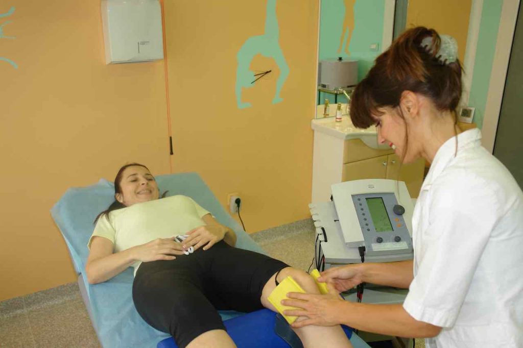 Fizioterapevt in pacient se smejita  med elektroterapijo za artritis kolena