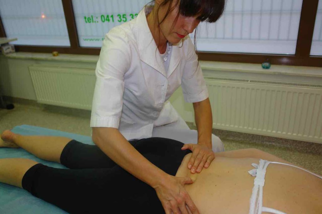 Fizioterapevt s palcem pritiska na hrbet v  smeri navzven za masažo vezivnih tkiv in sproščanje fascij